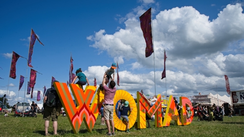 Children play on a large 3D sign which reads 'WOMAD' as adults help them on and off