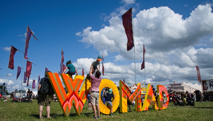 Children play on a large 3D sign which reads 'WOMAD' as adults help them on and off