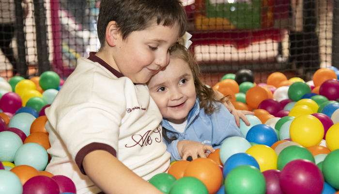 A young boy and a girl are close to each other and smiling in a soft play area ball pit