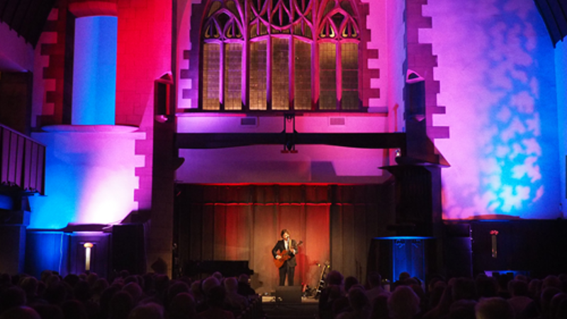 Live music performance on a stage inside a historic church venue, viewed from the audience seating area.