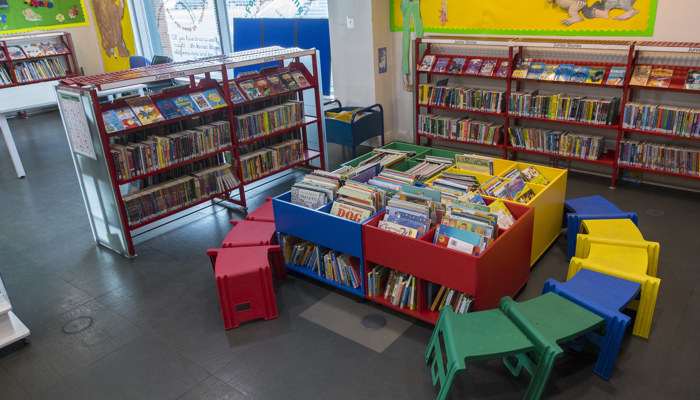 Brightly coloured children's section of Gorbals Library. Lots of boxes filled with picture books and red, yellow, blue and green coloured chairs.