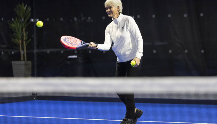 A woman hits a padel ball over the net on a padel court