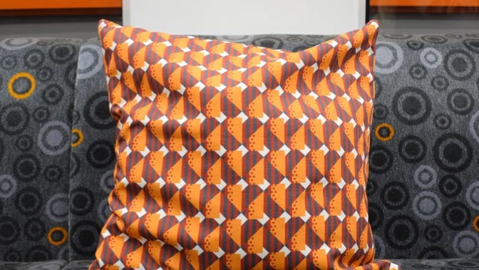 Patterned orange cushion on a grey upholstered seat with circular designs.