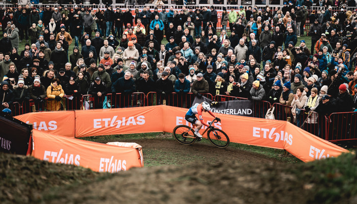 A cyclist races round a muddy track cheered on by spectators