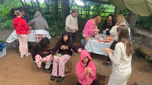 A group of young people taking part in an outdoor cooking activity in a large tent in a forest