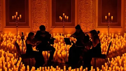 String quartet silhouetted against a backdrop of hundreds of orange-golden candles