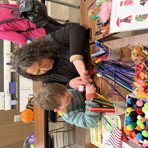 Adult and child taking part in a craft activity using colourful materials at a community workshop.