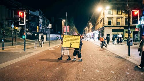 An image of two people walking across the street with a road sign. 