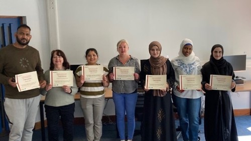A group of seven people holding certificates in a library computer room