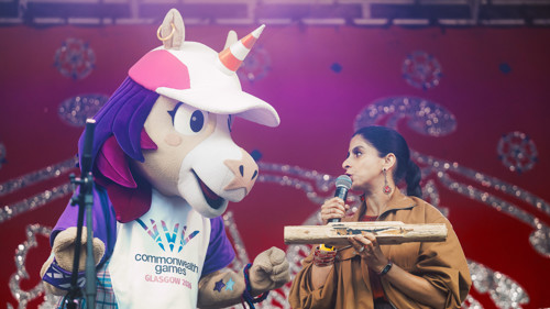 A musician is on stage with a person in a unicorn mascot outfit