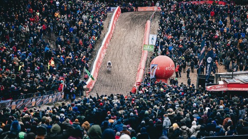 A cyclist races down a cyclo-cross track in front of a large crowd