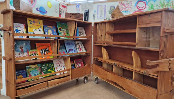 A wooden structure on wheels looking like a bookshelf, with a small table carved into its right hand side
