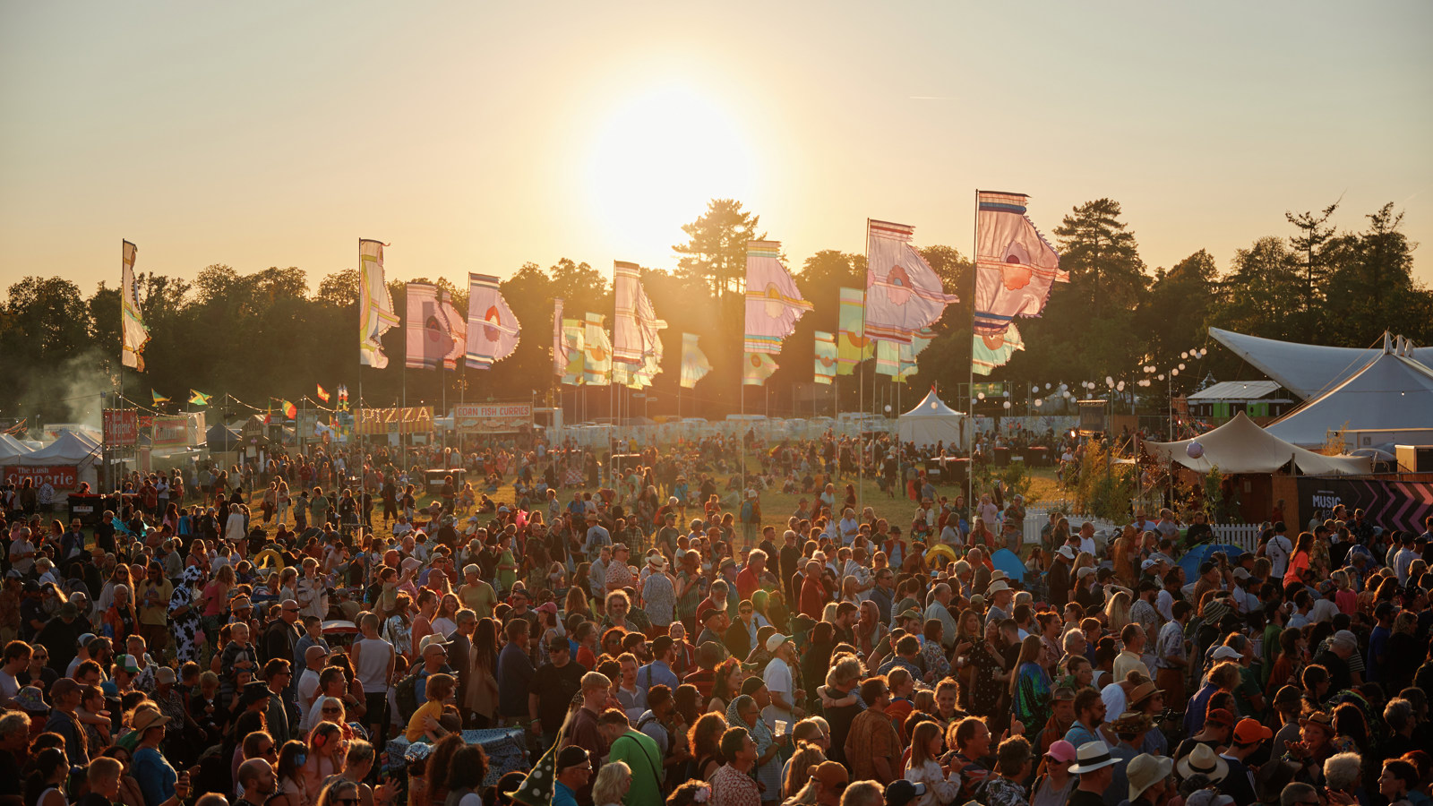 The sun shines over a large crowd at a music festival