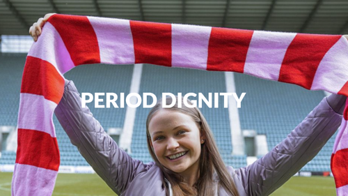 A young person with long hair holding up a striped football scarf on an outdoor football pitch