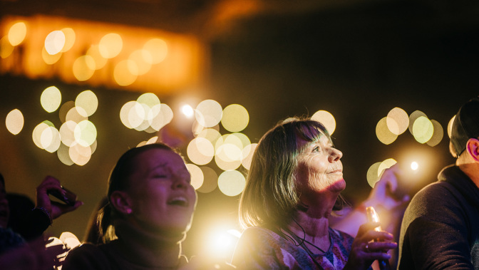 Audience watching a live music performance, illuminated by stage lighting and decorative lights.