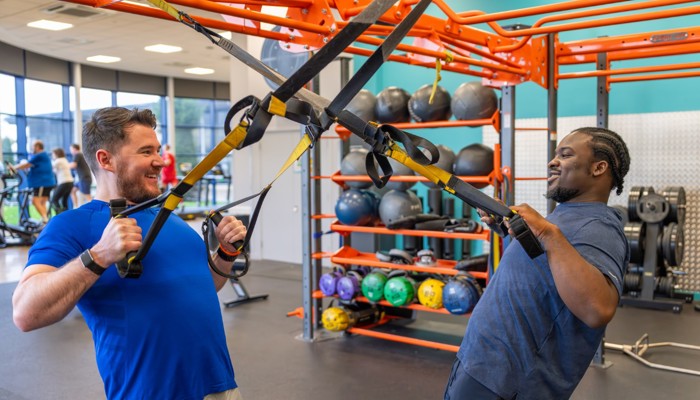 Two Glasgow Club members using TRX straps in gym they are facing each other and smiling