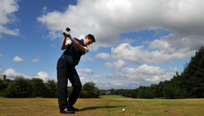 A person standing on grass swinging a golf club towards a golf ball.