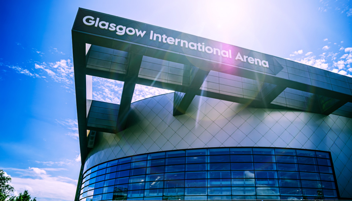Glasgow International Arena exterior with curved glass frontage and signage beneath a bright sunlit sky.