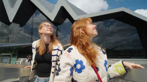 Two visitors take in their surroundings outside a museum with a modern wave-shaped frontage