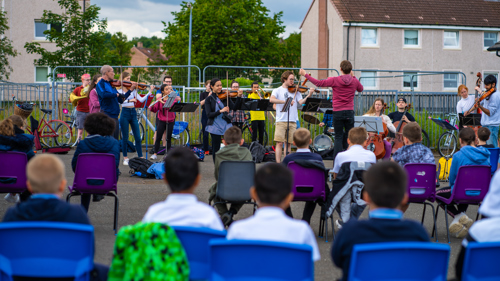 A band plays in a school playground with an audience.