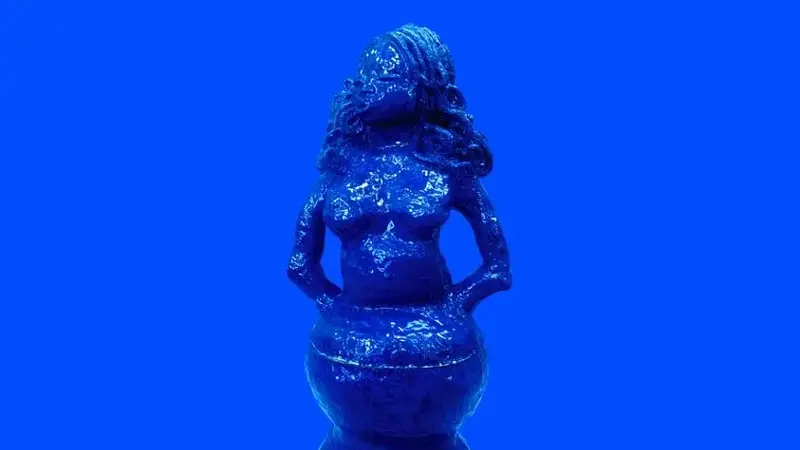 The photograph shows a striking, monochromatic blue sculpture set against a vibrant blue background, creating a seamless, almost surreal visual effect.  Because the background is the same colour, the figure appears to emerge from the space rather than simply sit within it
