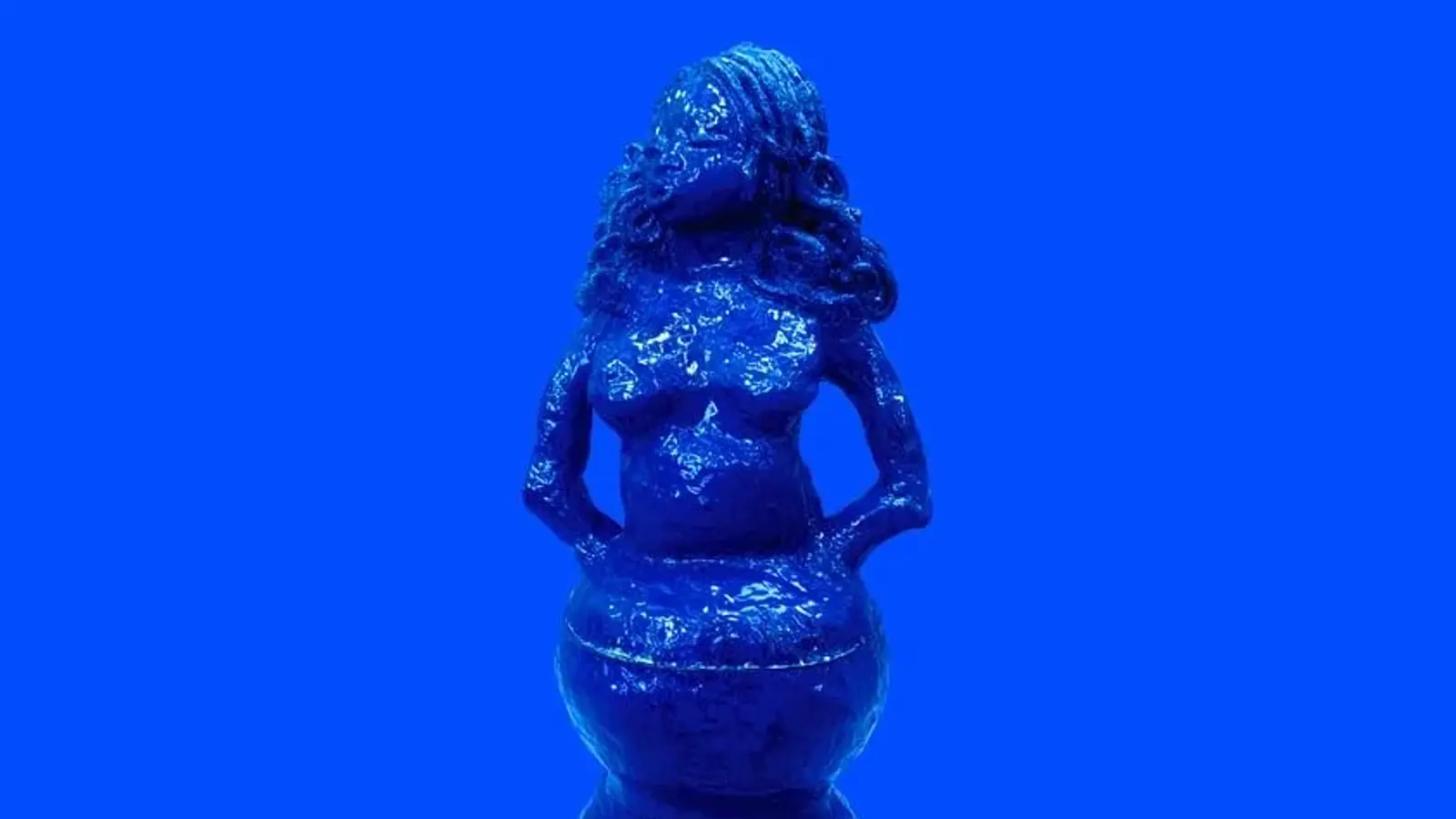 The photograph shows a striking, monochromatic blue sculpture set against a vibrant blue background, creating a seamless, almost surreal visual effect.  Because the background is the same colour, the figure appears to emerge from the space rather than simply sit within it