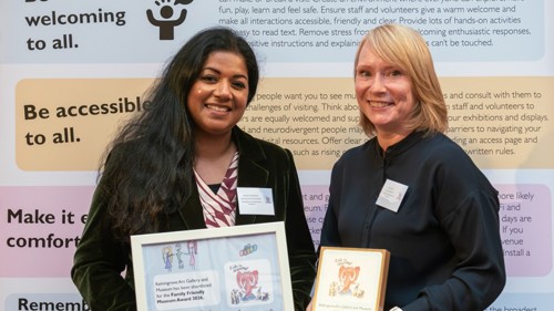Two people smiling and holding framed award certificates