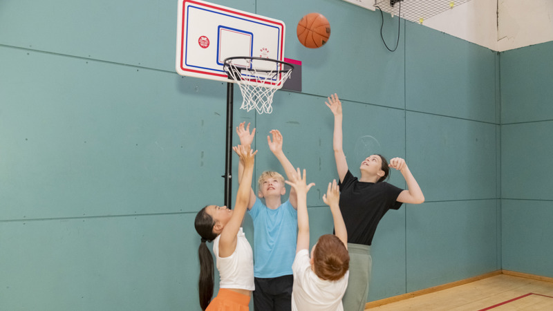 A group of children are playing basketball and jumping up towards a basketball net