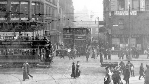 Black and white image showing a glasgow street scene from early 1900s, people are milling in the street and there is a tram