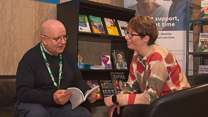 Two people sitting looking at each other smiling with leaflet in hand