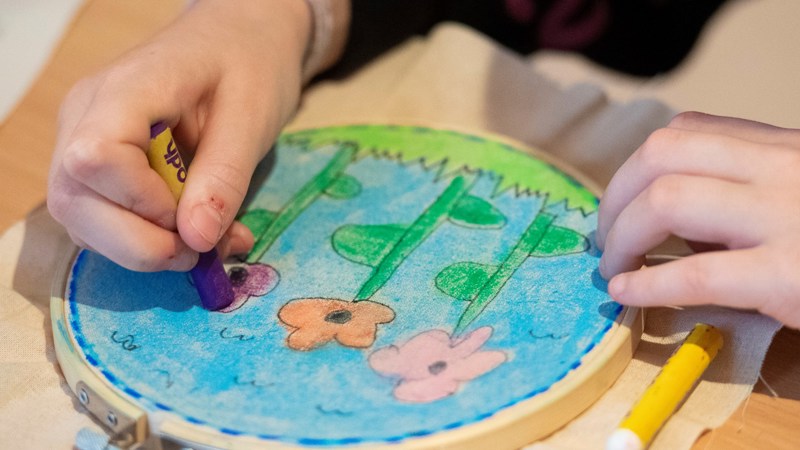 A child's hands are shown using crayons to colour in some flowers