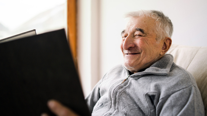 A close up shot of an elderly man smiling while holding and reading a book