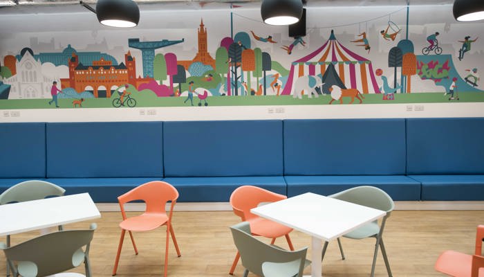 Tables with bright orange and green chairs with a colourful circus themed murals on the back wall