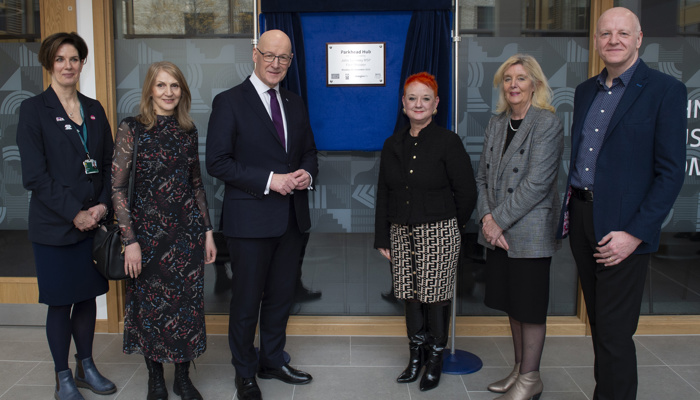 Six people stand either side of a plaque commemorating the official opening of a health, social care and community facility