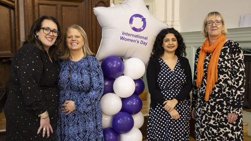 A group of four people smiling for a photo next to a star shaped balloon with text International Women's Day