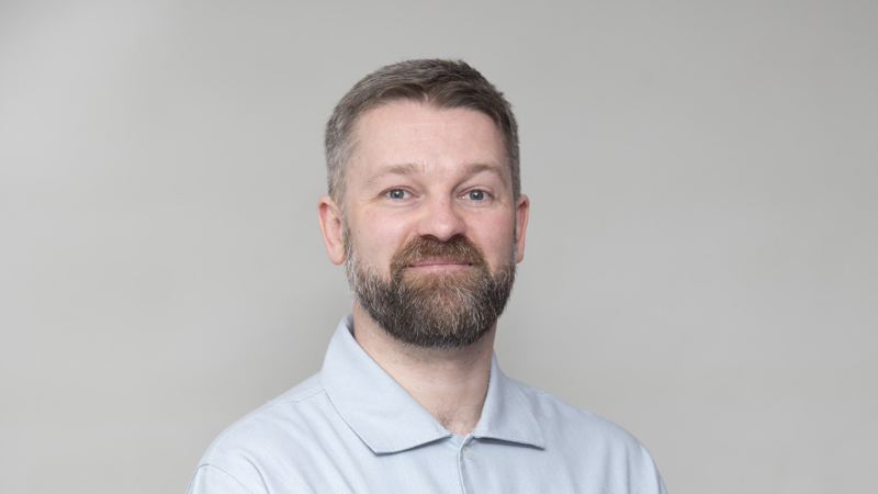 Headshot of a person with short hair and beard, wearing a light shirt, against a neutral background.