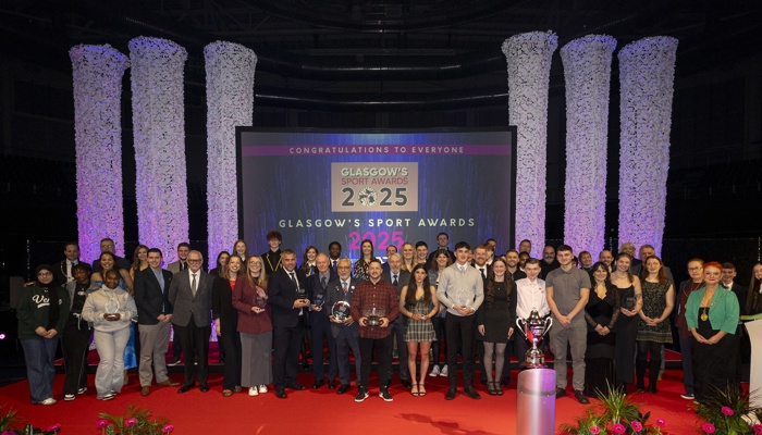 People stand on a red carpet in front of a large screen at an awards ceremony
